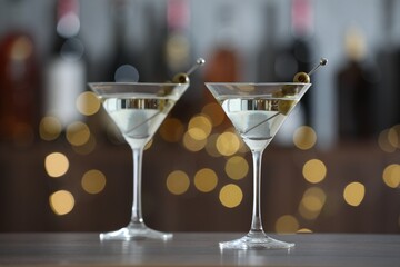 Martini cocktail with olives in glasses on wooden table against blurred background. Bokeh effect