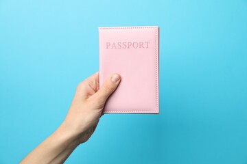 Fototapeta premium Woman holding passport in bright cover on light blue background, closeup
