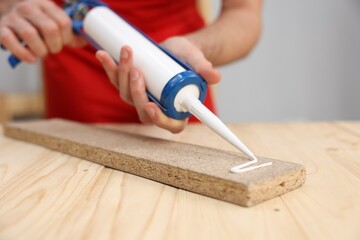 Man with caulking gun glueing wooden plank at table, closeup