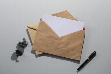 Kraft paper envelopes with letter, fountain pen and eucalyptus branch on grey background, flat lay....