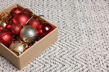 Shiny tinsel and Christmas balls in cardboard box on carpet, space for text