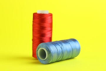 Spools of colorful sewing threads on yellow background, closeup
