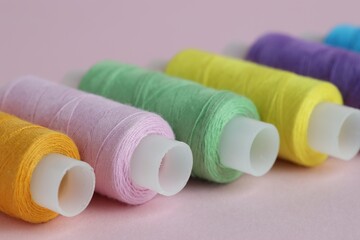 Spools of colorful sewing threads on pink background, closeup