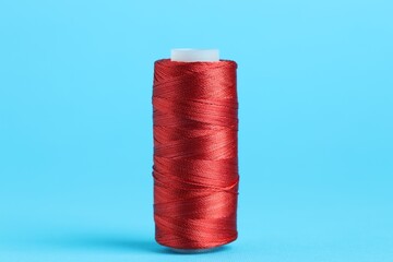 Spool of red sewing thread on light blue background