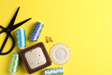 Different sewing supplies on yellow background, flat lay. Space for text