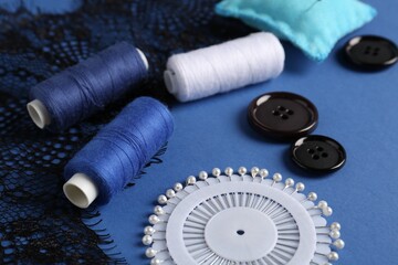 Different sewing supplies on blue background, closeup