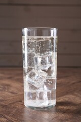 Refreshing soda water with ice cubes in glass on wooden table, closeup