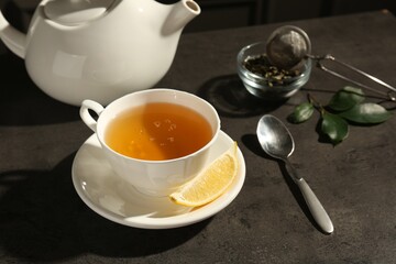 Refreshing green tea in cup and slice of lemon on dark textured table