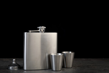 Hip flask, cups and funnel on grey table, space for text