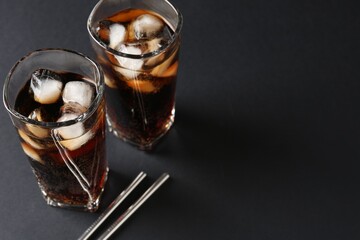 Refreshing cola with ice cubes in glasses and drinking straws on black table, closeup. Space for text