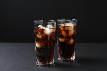 Refreshing cola with ice cubes in glasses on black table, closeup