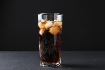 Refreshing cola with ice cubes in glass on black table, closeup