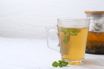 Aromatic mint tea and fresh leaves on white textured table, closeup. Space for text