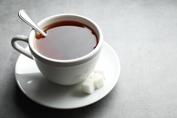 Refreshing black tea in cup and sugar cubes on grey textured table, closeup. Space for text