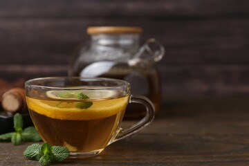 Tasty mint tea in cup, lemon and fresh leaves on wooden table, closeup. Space for text