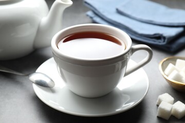 Refreshing black tea in cup and sugar cubes on grey textured table, closeup