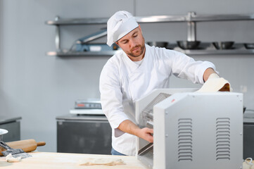 Traditional italian food. Side view of handsome chef rolling a dough through pasta machine in the...