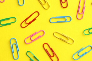 Colorful paper clips on yellow background, flat lay