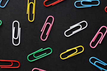 Colorful paper clips on black background, flat lay