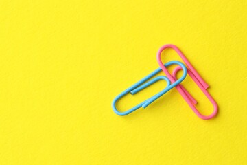 Two paper clips on yellow background, top view. Space for text