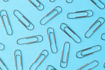 Metal paper clips on light blue background, flat lay