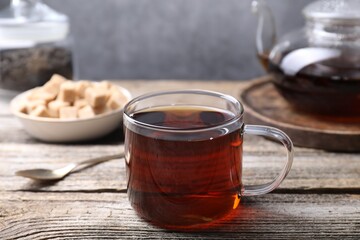 Aromatic black tea in cup and spoon on wooden table, closeup