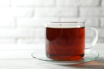 Aromatic black tea in cup on white wooden table, closeup. Space for text