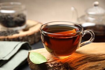 Aromatic black tea in cup and green leaf on wooden snag, closeup