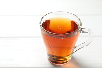 Aromatic black tea in cup on white wooden table, closeup. Space for text