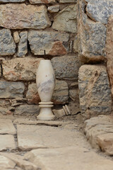 A weathered marble artifact rests against a rustic stone wall at an archaeological site, showcasing historical craftsmanship and ancient architecture.  
