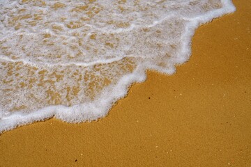 The photo captures a soft wave of the sea gently lapping at the sandy beach, creating a soothing rhythm that invites relaxation and enjoyment of nature s beauty.