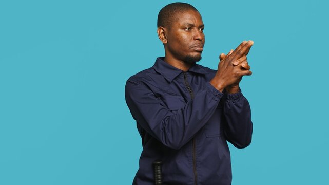 Portrait of security agent securing assigned post, pretending to shoot gun, studio background. African american guardian prepared to handle security breaches, doing pistol fingers gesturing, camera A