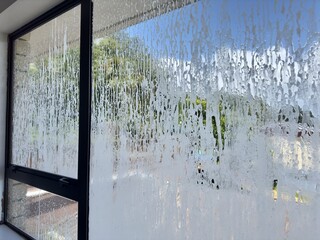 An aluminum-framed residential window as seen from inside the home, covered in a layer of suds...
