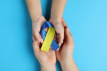 Woman with child holding yellow and blue ribbons on color background, top view. Down syndrome...