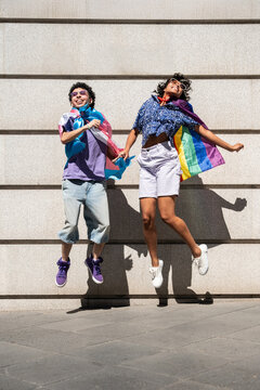 Happy LGBTQ+ couple celebrates diversity jumping with pride flags