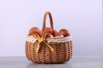 Wicker basket with fresh eggs on grey marble table against white background, closeup