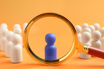 Looking at blue human figure through magnifying glass among other ones against orange background, closeup. Competition concept