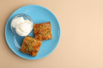 Tasty baklava with chopped nuts and scoops of ice cream on beige table, top view. Space for text