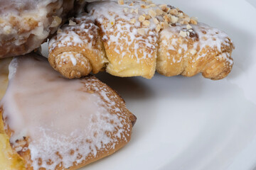 A close up of freshly baked pastries, including croissants and buns, covered with sugar icing and sprinkled with crushed nuts.