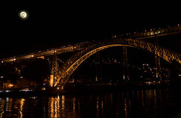 Metallic bridge in the city of Porto at night with lighting on and full moon in the sky. Douro river downtown Porto, Dom Luís Bridge, Portugal