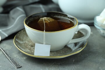 Tea bag in cup with hot drink on gray textured table, closeup