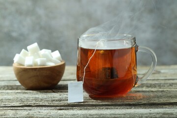 Tea bag in glass cup with hot drink and sugar cubes on wooden table against gray background