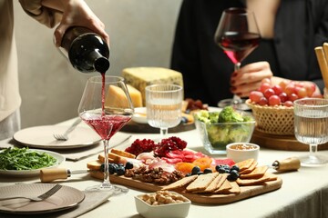 Woman pouring wine into glass at table with different snacks indoors, closeup