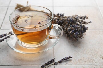 Aromatic lavender tea in glass cup and dry flowers on white tiled table, closeup