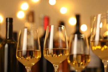 Tasty white wine in glasses against blurred background with festive lights, closeup. Bokeh effect