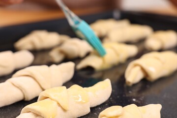 Woman brushing egg wash onto raw croissants at table indoors, closeup