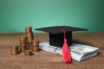 Graduate hat, dollar banknotes and coins on wooden table, closeup. Tuition payment