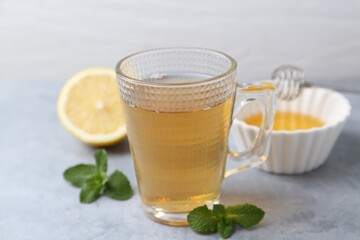 Aromatic mint tea in glass cup, fresh leaves and lemon on light gray table, closeup