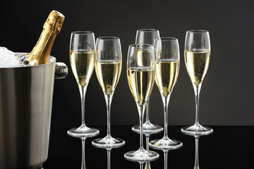 Bottle of sparkling wine in cooler bucket and glasses on black mirror surface