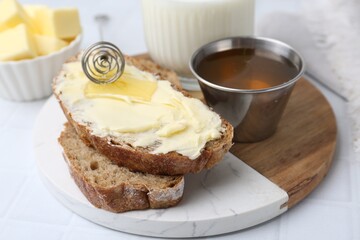Slices of bread with butter, honey and milk on white tiled table, closeup